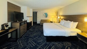 Una habitación de hotel con una cama, televisión, escritorio, silla y lámpara.