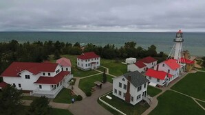 Una zona costera con edificios blancos de techos rojos, un faro y vista al mar.
