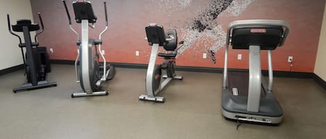 Un gimnasio con tres bicicletas estáticas y una cinta de correr.