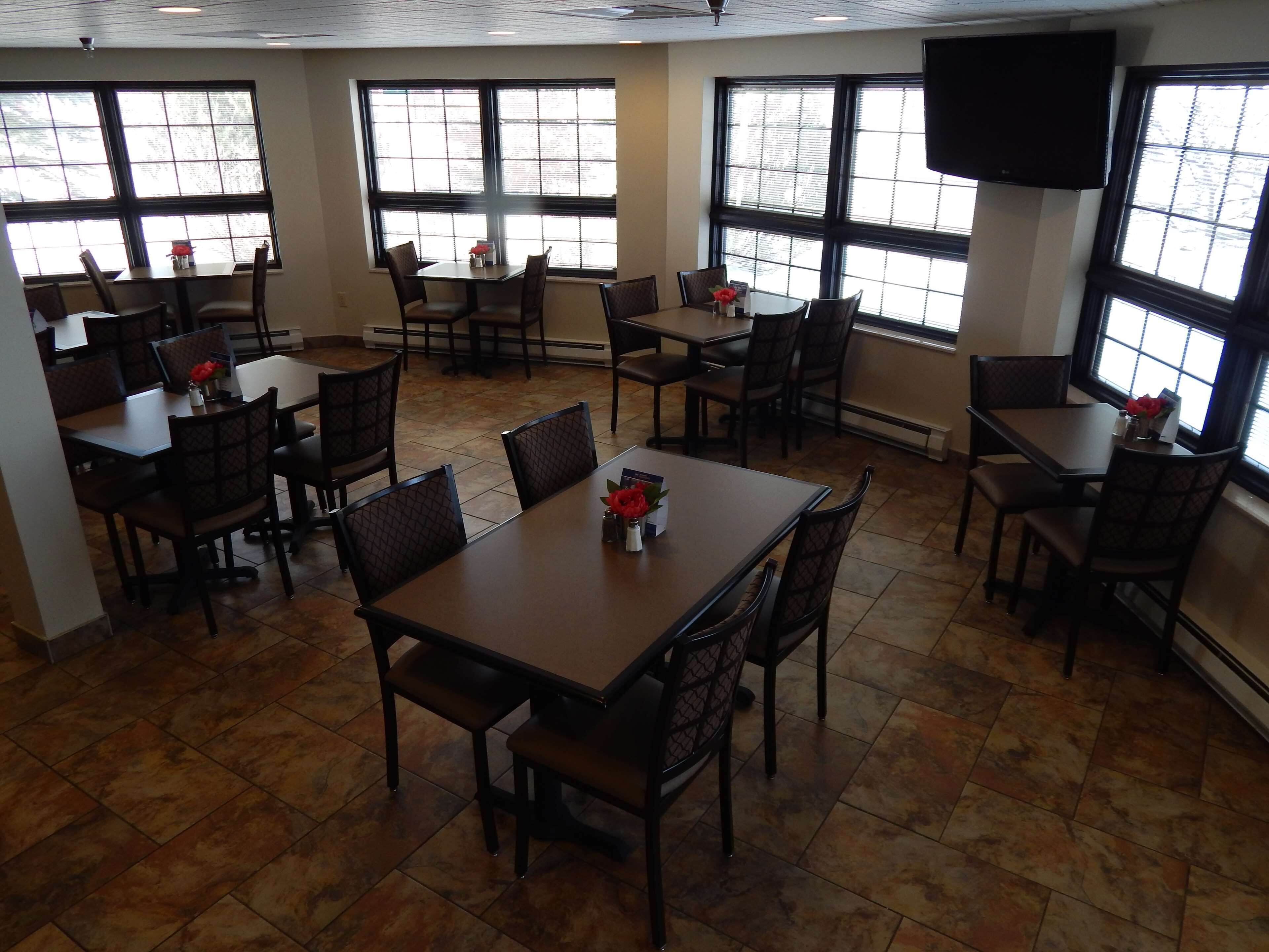 A restaurant with multiple tables and chairs, large windows, and a flat-screen TV mounted on the wall.