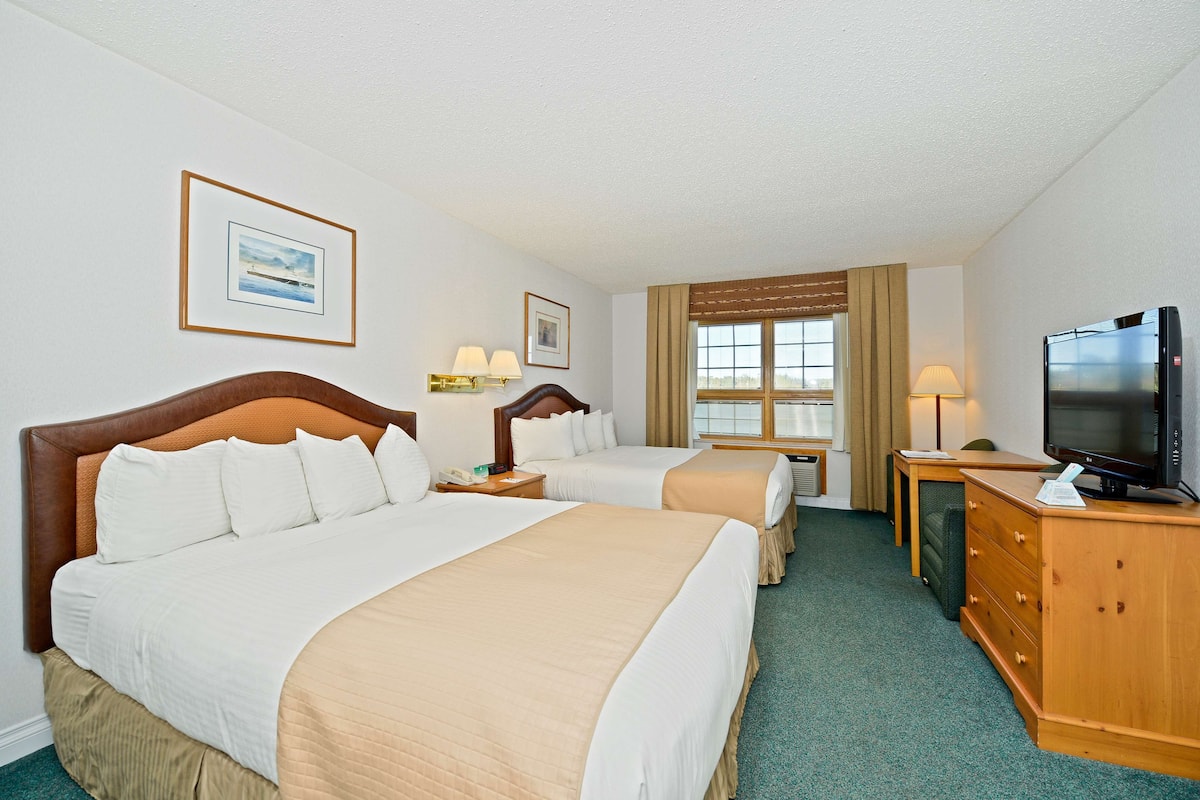 A hotel room with two beds, a television, a desk, and a window.