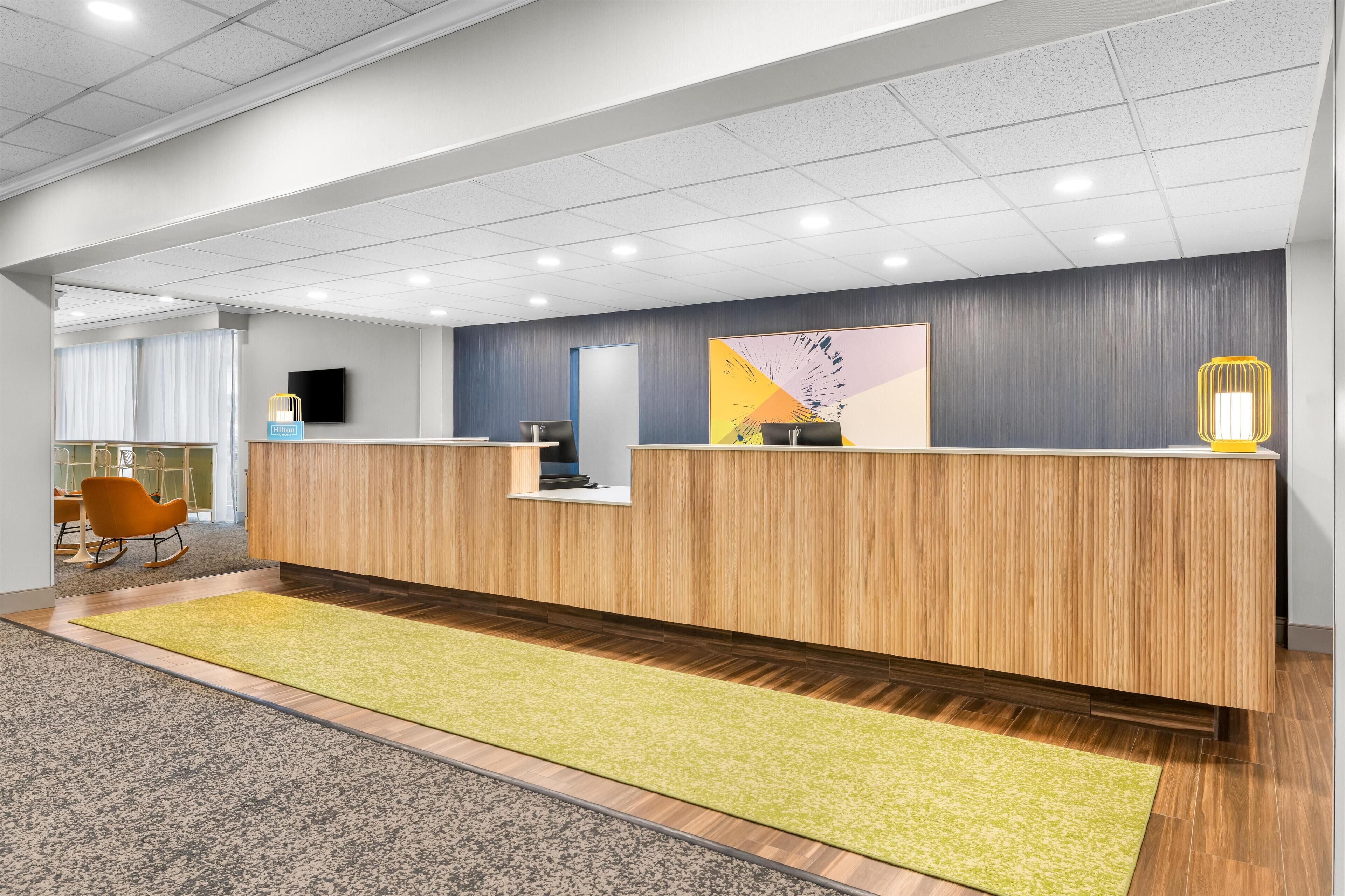 A reception area with a wooden reception desk, a yellow rug, and a television mounted on the wall.