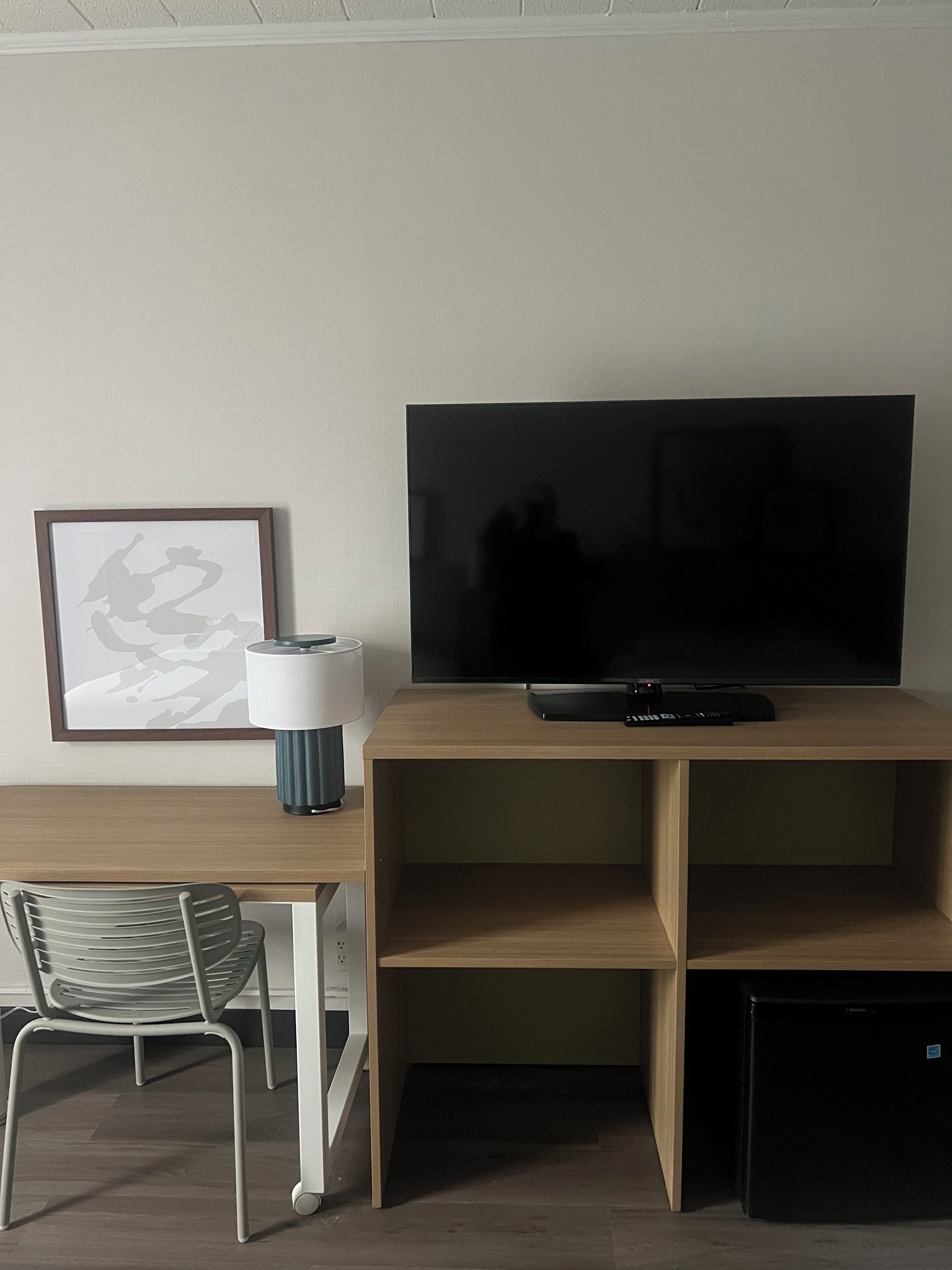 Un salon moderne avec un téléviseur à écran plat posé sur un meuble en bois, une œuvre d’art encadrée accrochée au mur, une lampe, un fauteuil et un petit appareil électroménager noir.