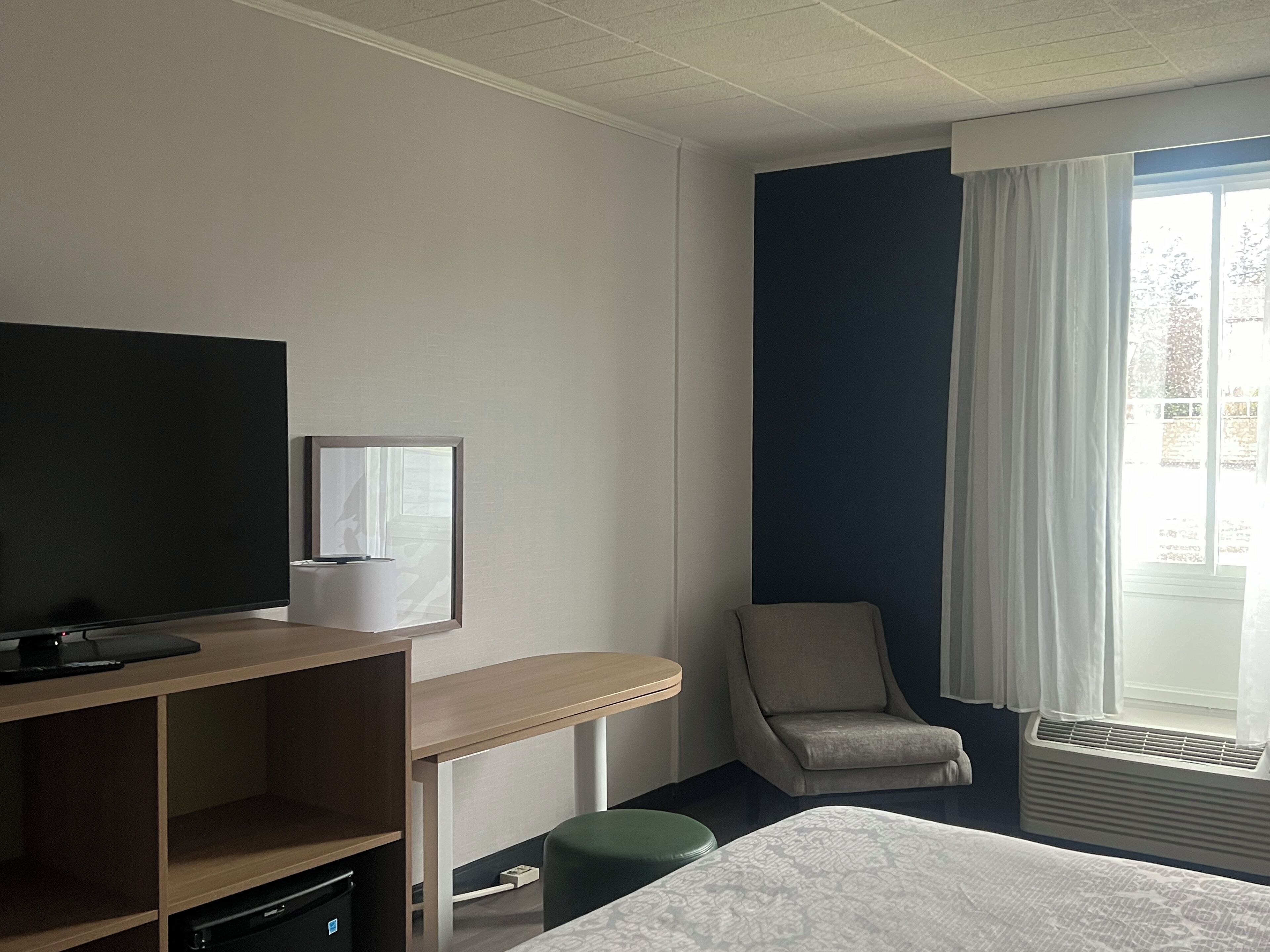 A hotel room with a bed, a desk, a chair, a TV, and a window with curtains.