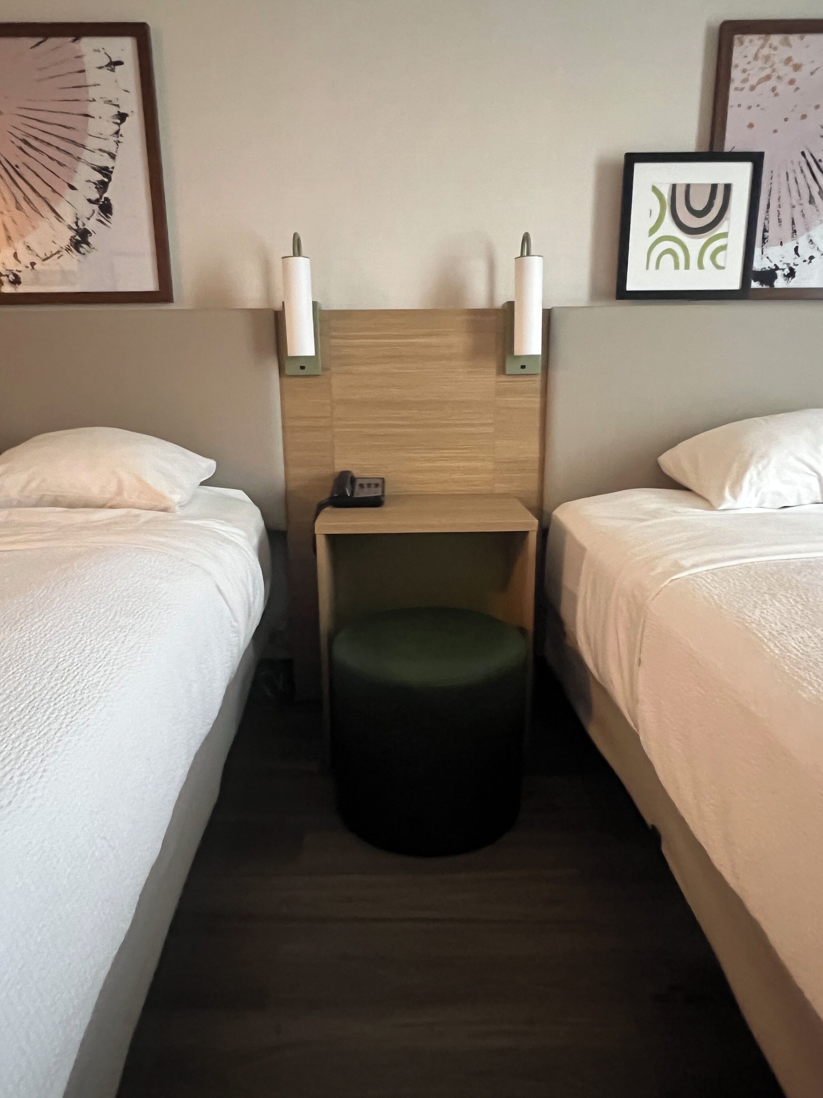 A hotel room with two single beds, a small wooden nightstand with a phone, and wall-mounted lamps.