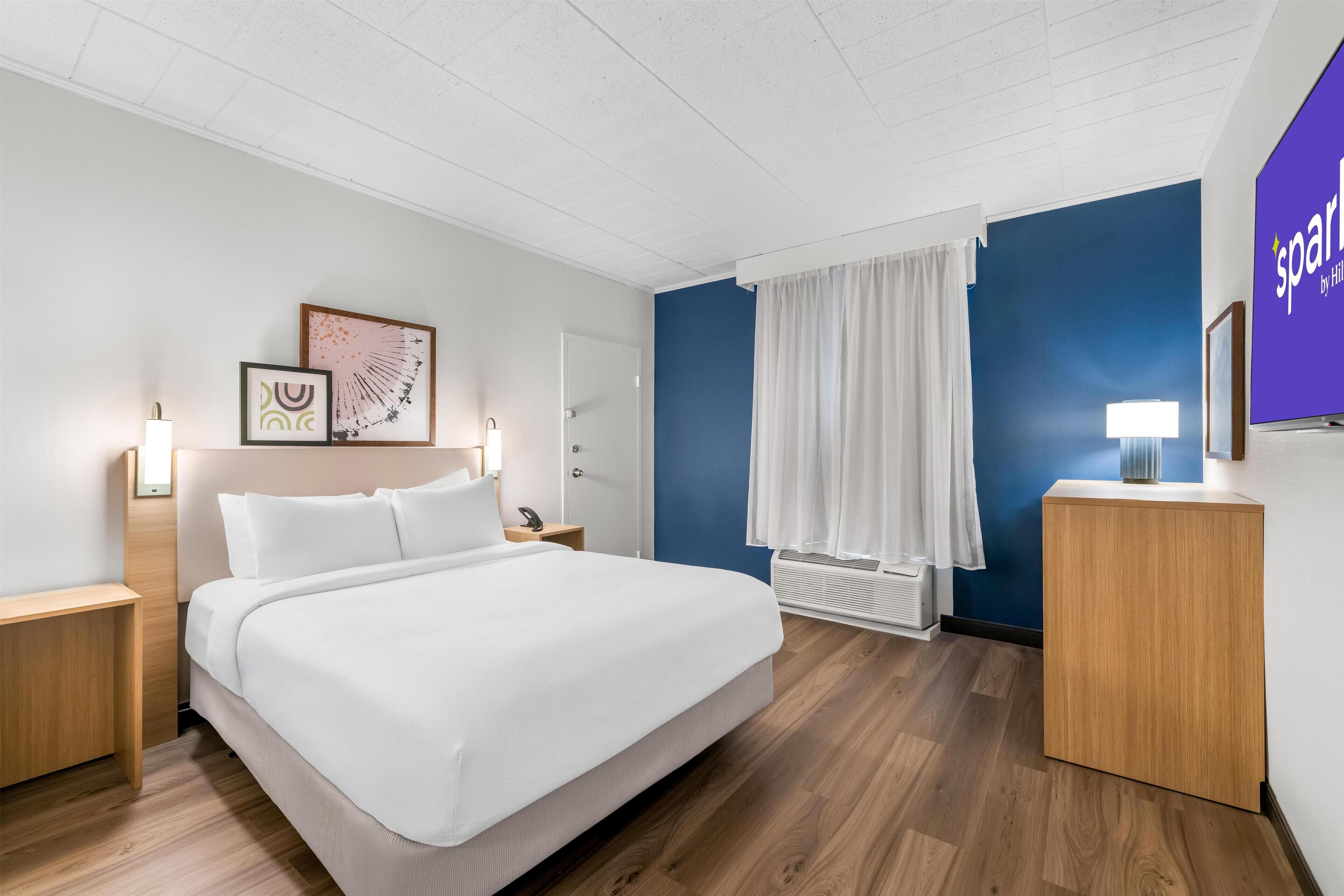A modern hotel room with a large bed, bedside tables, a flat-screen TV, and artwork on the walls.