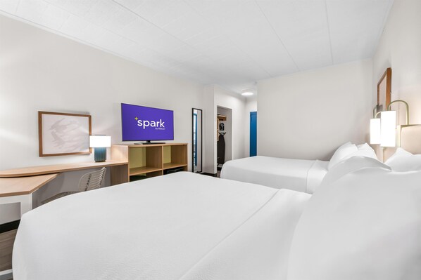 A hotel room with two beds, a desk with a computer, a TV displaying 'spark by Hilton', and a wardrobe.