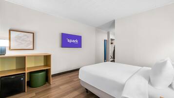 A modern hotel room with a bed, a desk, a small refrigerator, and a trash bin.