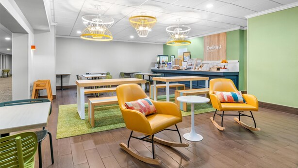 Een modern interieur met gele schommelstoelen, een houten tafel en een groene wand met een 'Delight' bord.