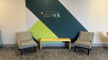 A room with two armchairs, a small table, and a wall with a geometric design and the text "It only takes a spark".
