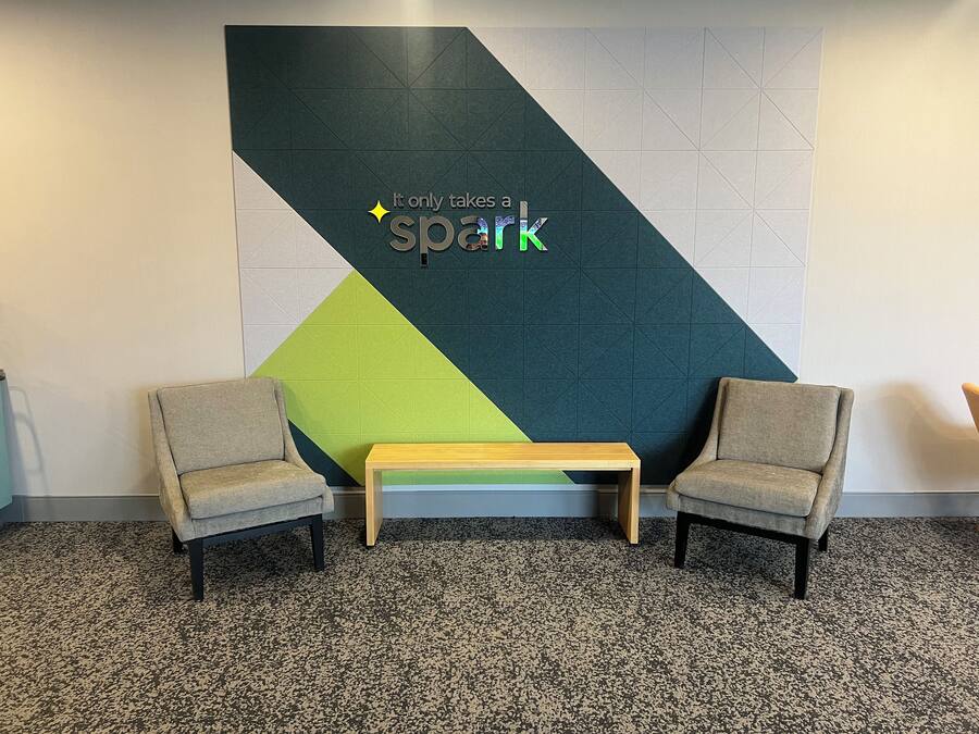 A room with two armchairs, a small table, and a wall with a geometric design and the text "It only takes a spark".