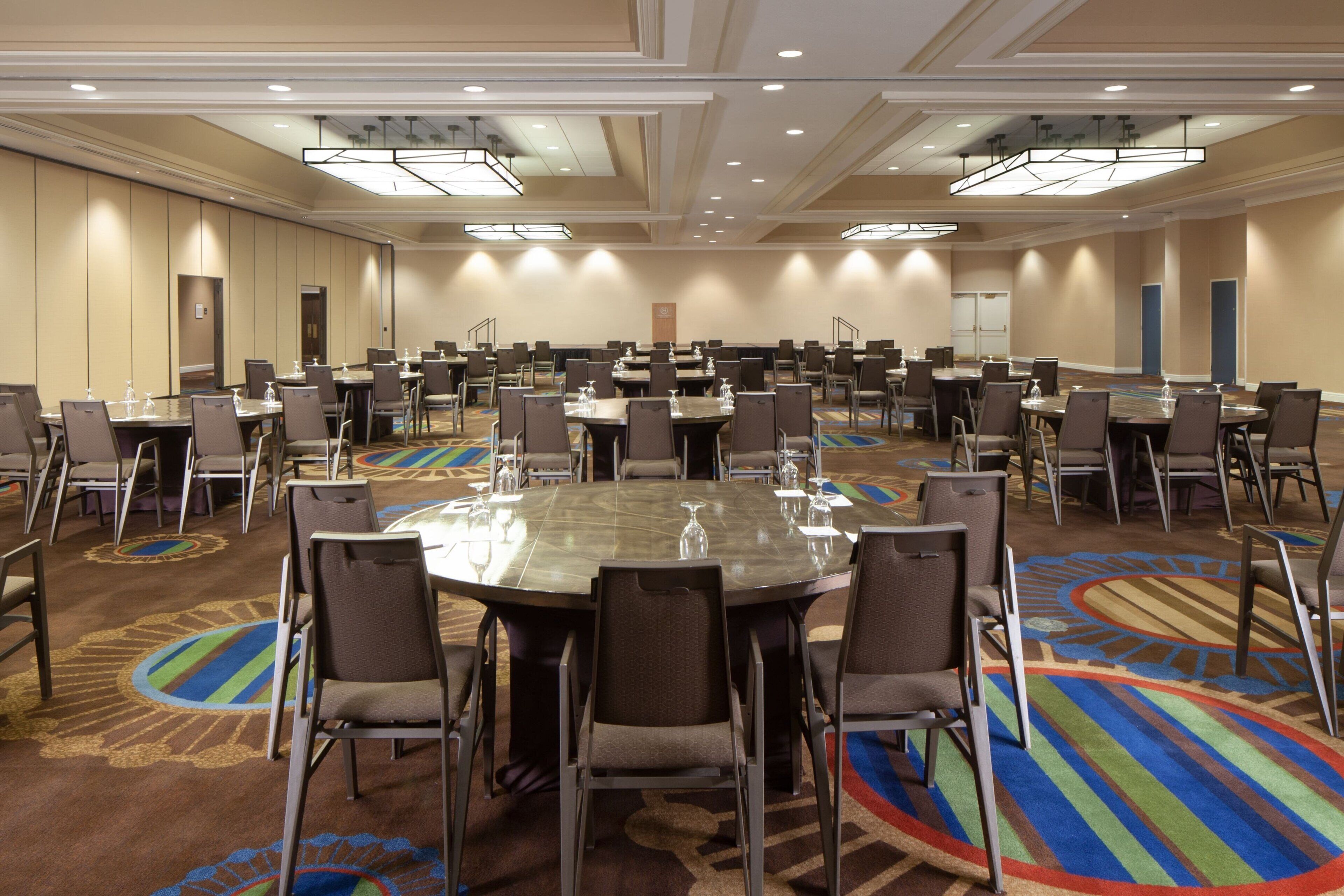 A large conference room with multiple tables and chairs, carpeted floor, and ceiling lights.
