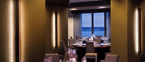 A well-lit dining area with a table set for a meal, large windows offering a view, and textured walls.