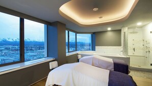 Een moderne hotelkamer met een groot raam met uitzicht op de stad, een aparte douche en een bed met een wit en paars dekbed.
