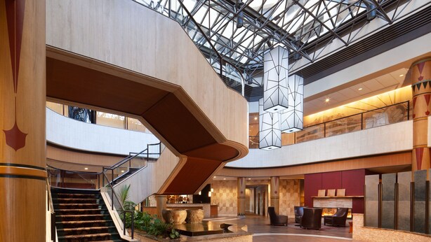 Een ruime lobby met een centrale trap, een receptiebalie en een zithoek.