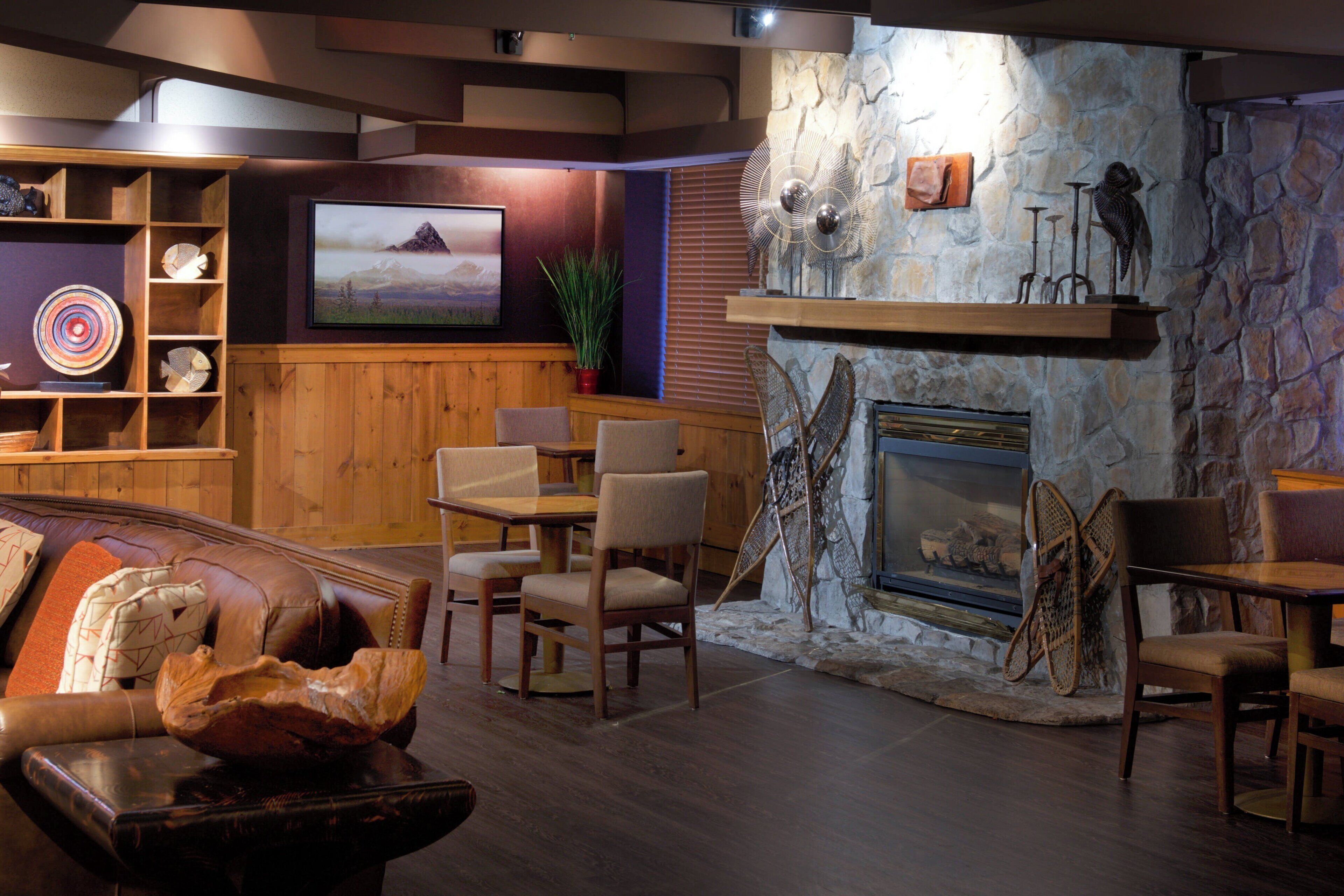 A cozy lounge area with a stone fireplace, wooden furniture, a mounted TV, and a decorative wall.