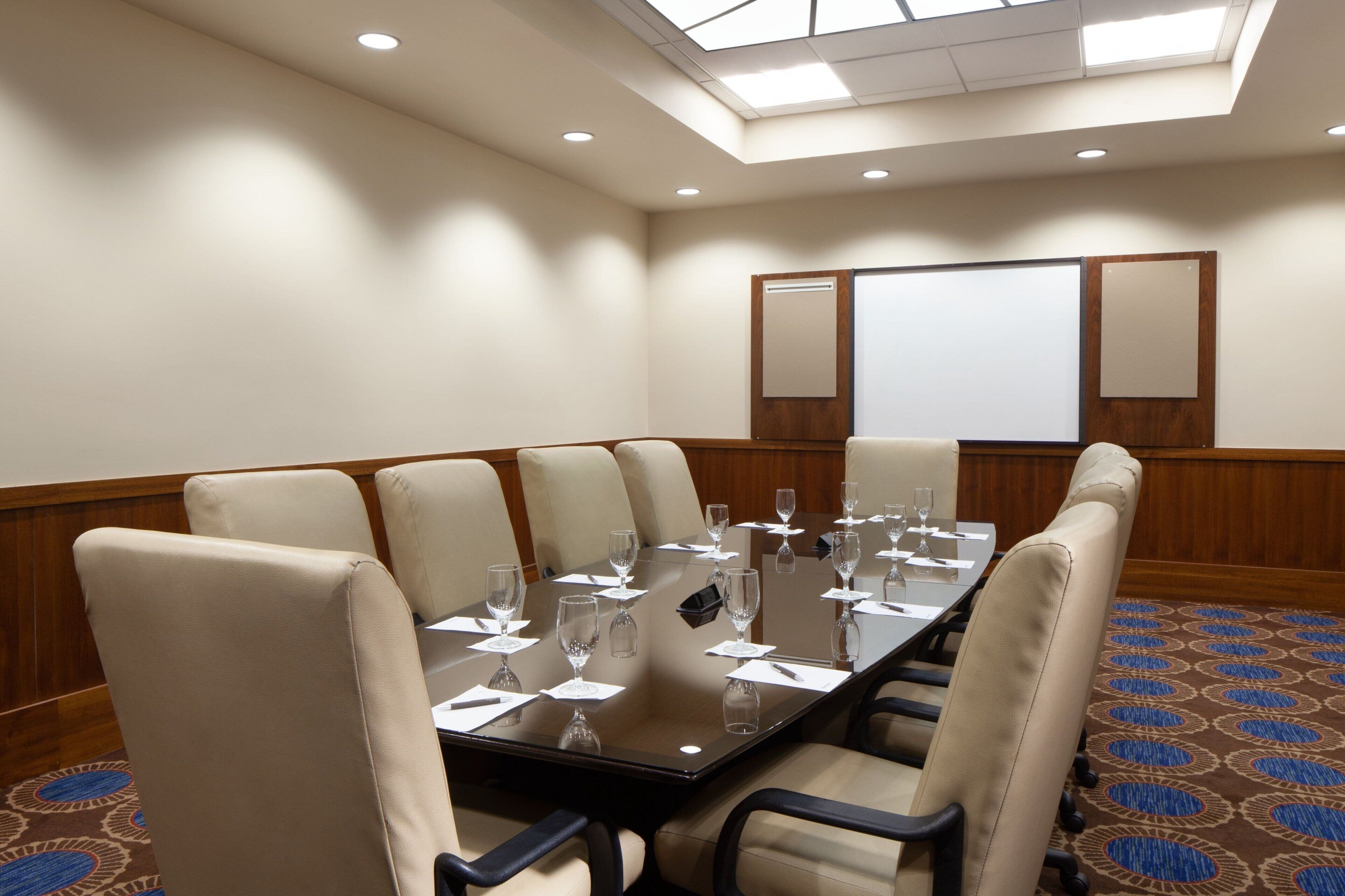 A conference room with a long table, six chairs, and a projector screen on the wall.