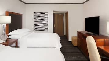 Una habitación de hotel con una cama, un escritorio con televisor, una silla, una lámpara y un cuadro en la pared.
