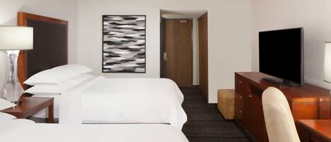 Una habitación de hotel con una cama, un escritorio con televisor, una silla, una lámpara y un cuadro en la pared.