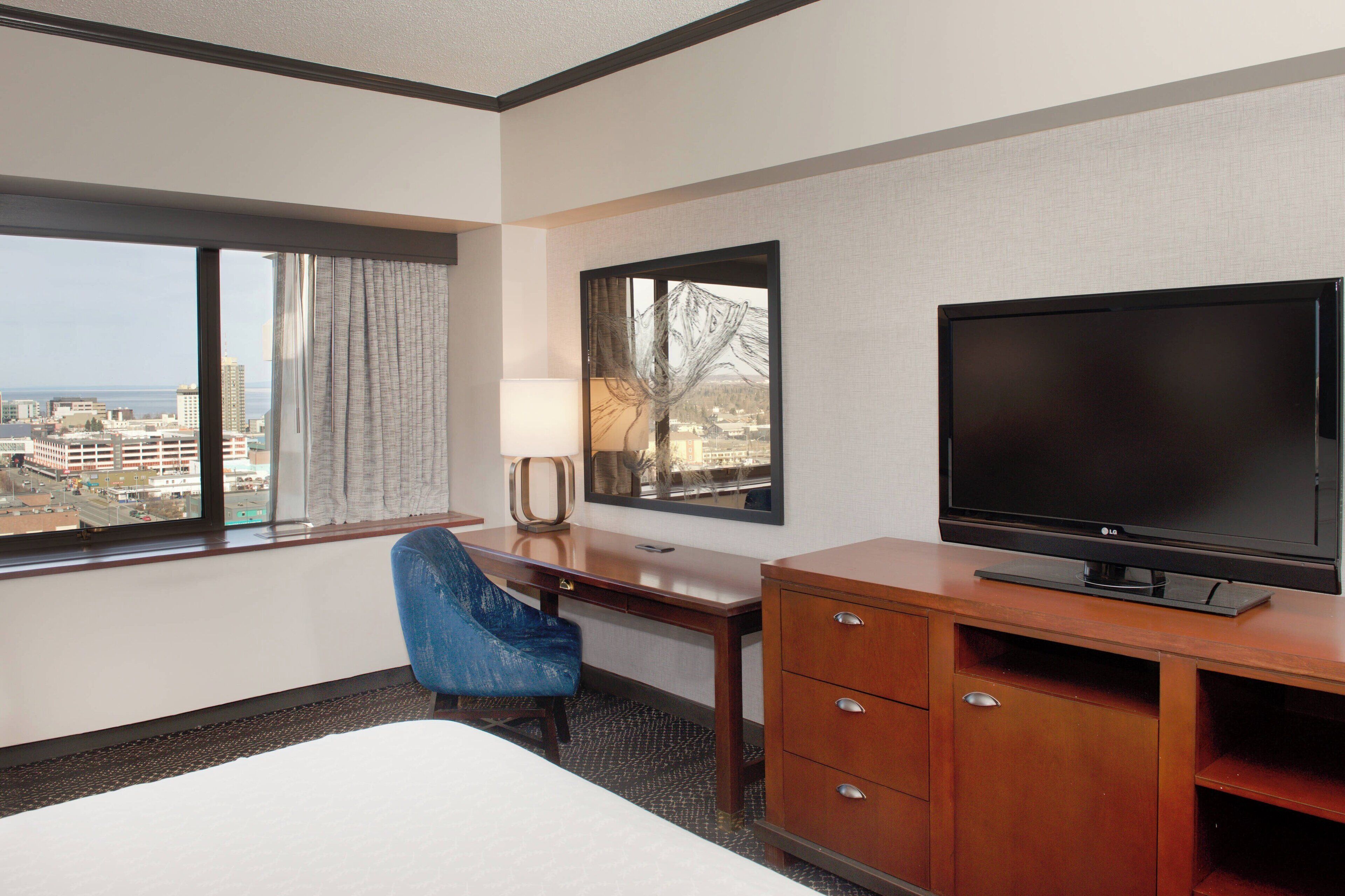 Une chambre d’hôtel avec un lit, un bureau, une télévision, une chaise et une vue sur la ville.