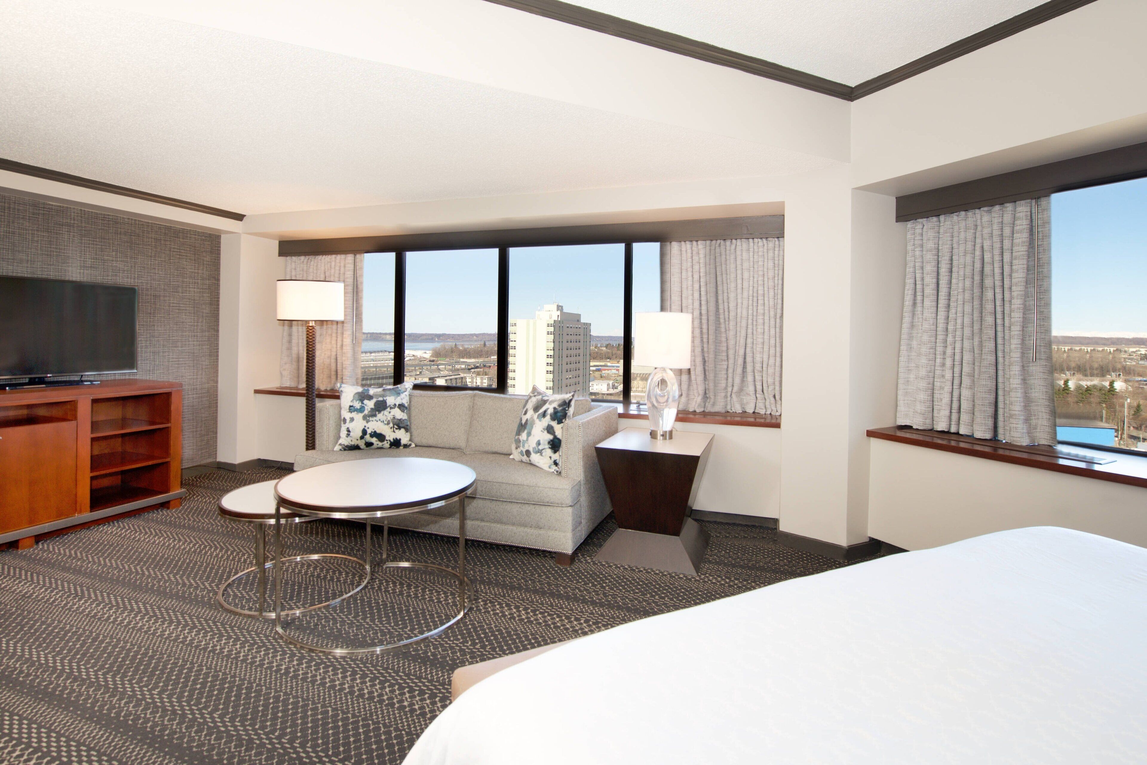 Habitación de hotel con cama, televisión, sofá, una mesita y vistas de la ciudad.