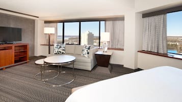 Habitación de hotel con cama, televisión, sofá, una mesita y vistas de la ciudad.
