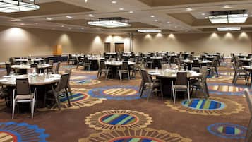 Une grande salle de conférence dotée de nombreuses tables et chaises, d’un sol recouvert de moquette orné de motifs circulaires et d’un éclairage au plafond.