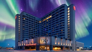Een hotel met een modern design, met een opvallend logo op de gevel, een ruime entree en een parkeerplaats ervoor.