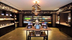 Een goed verlichte winkel met schappen vol verschillende producten, een centrale display tafel met artikelen en een moderne kroonluchter.