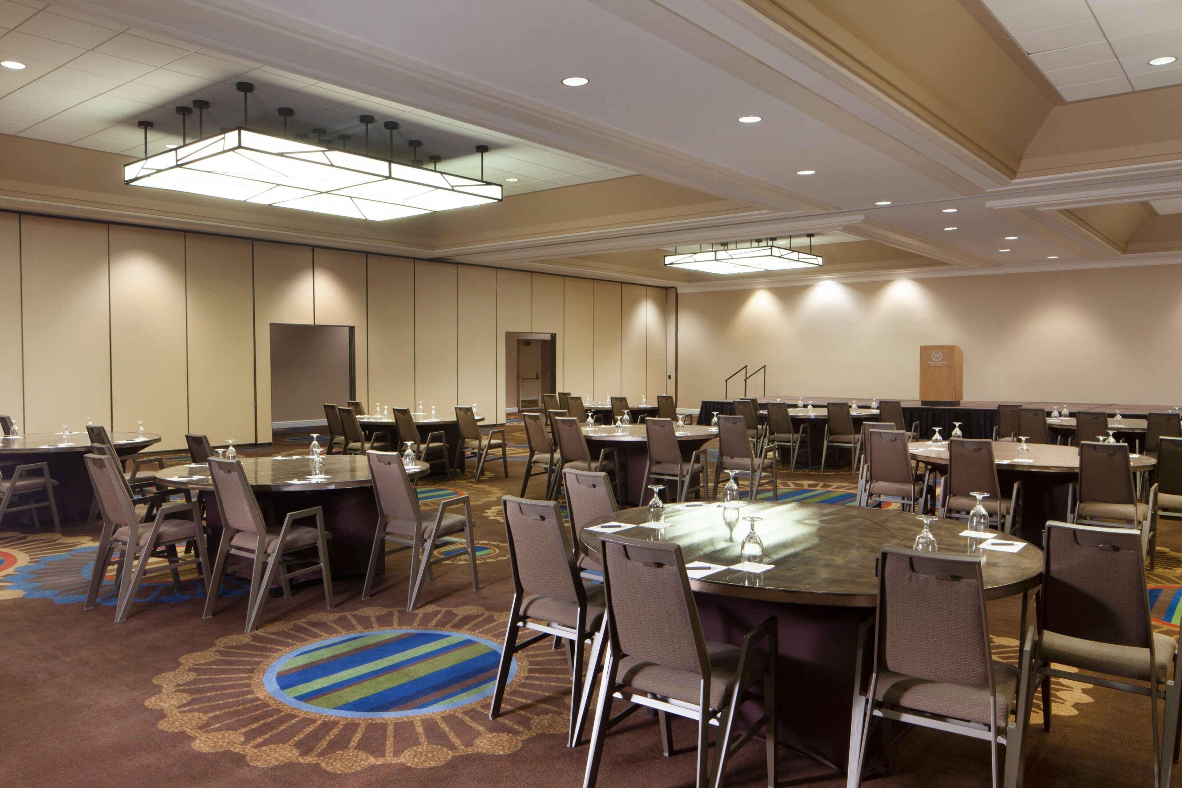 A conference room with multiple tables and chairs, equipped with water glasses and microphones.