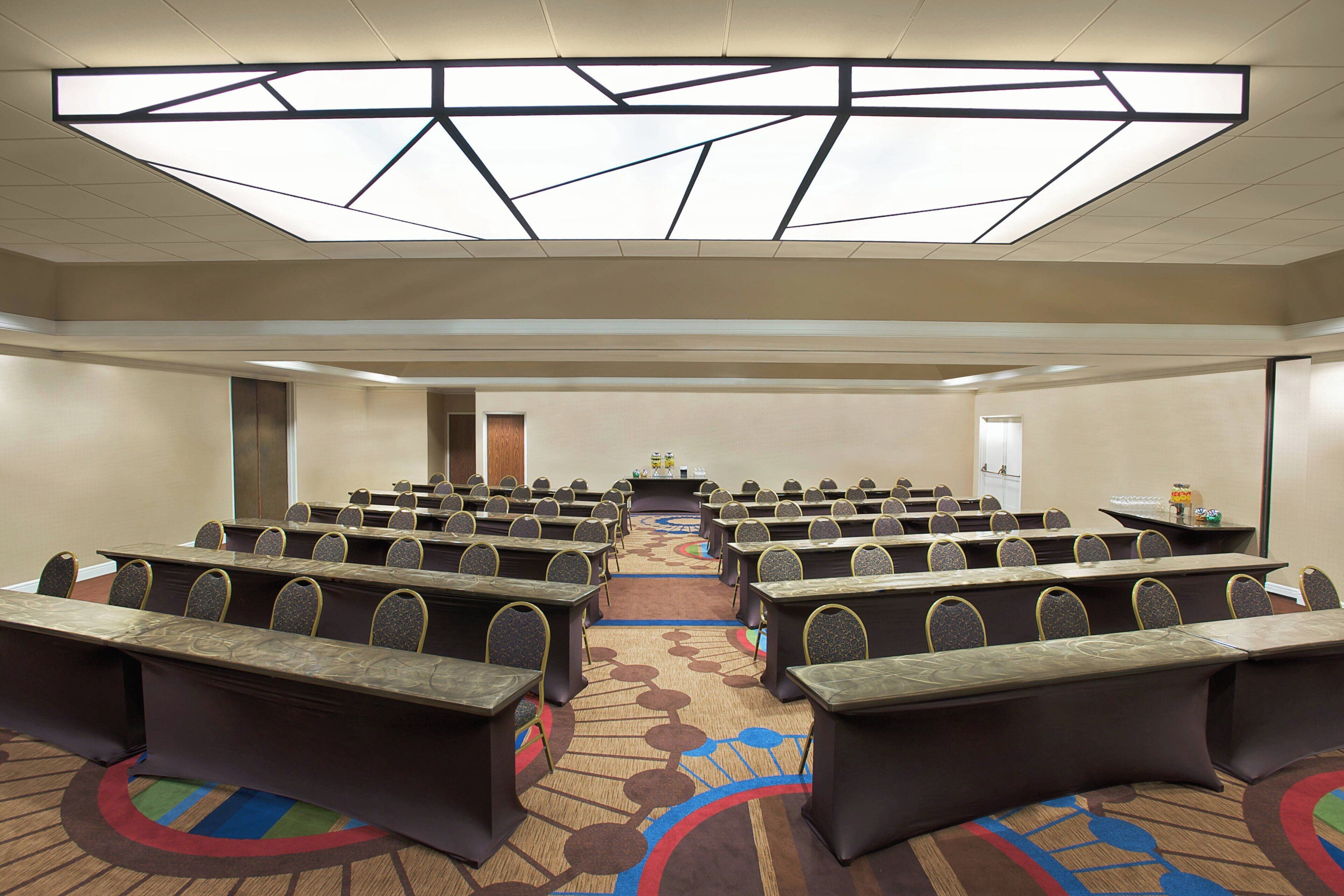 A conference room with rows of tables and chairs, a podium, and a carpeted floor.