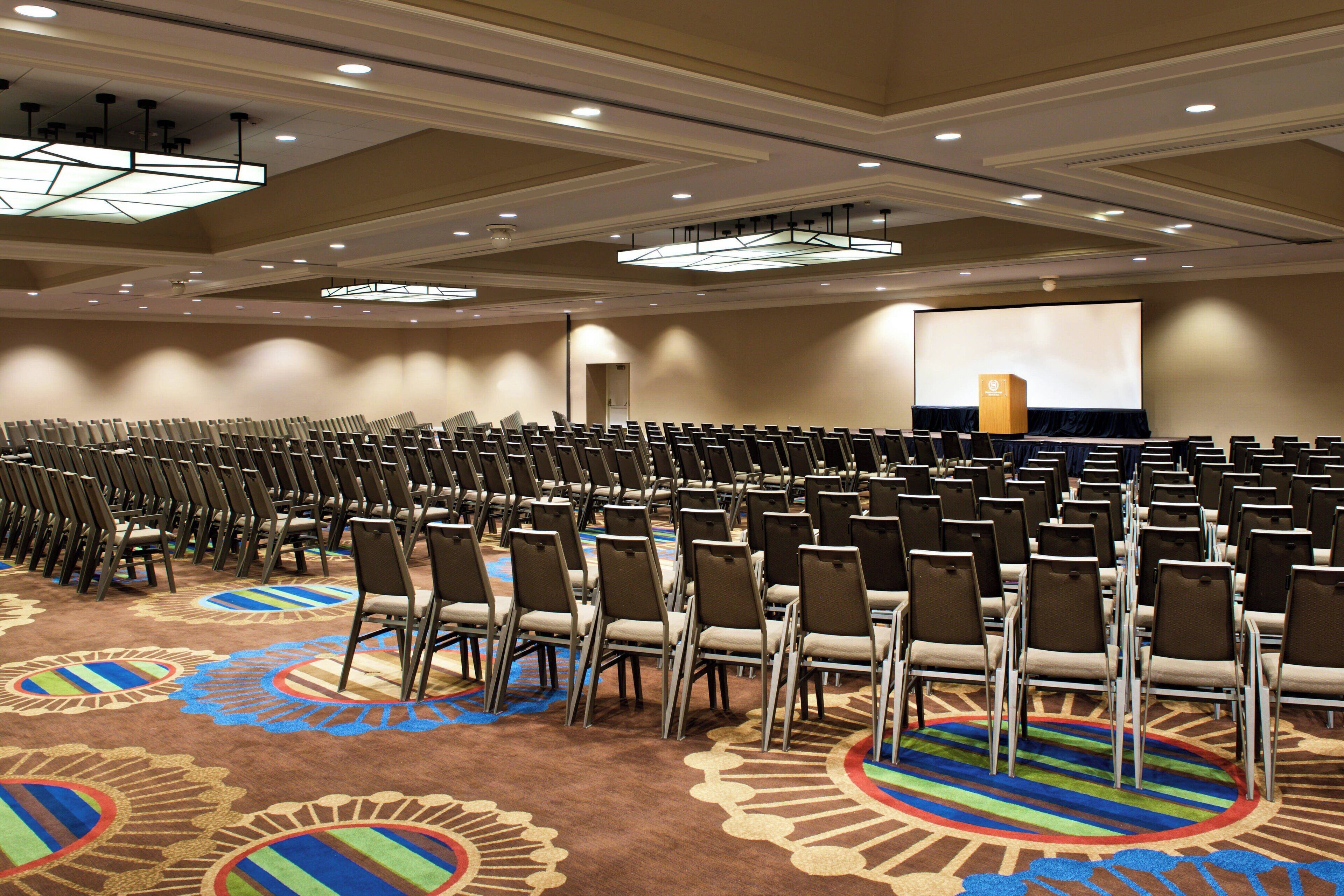A conference room with rows of chairs, a large screen, and a carpeted floor.