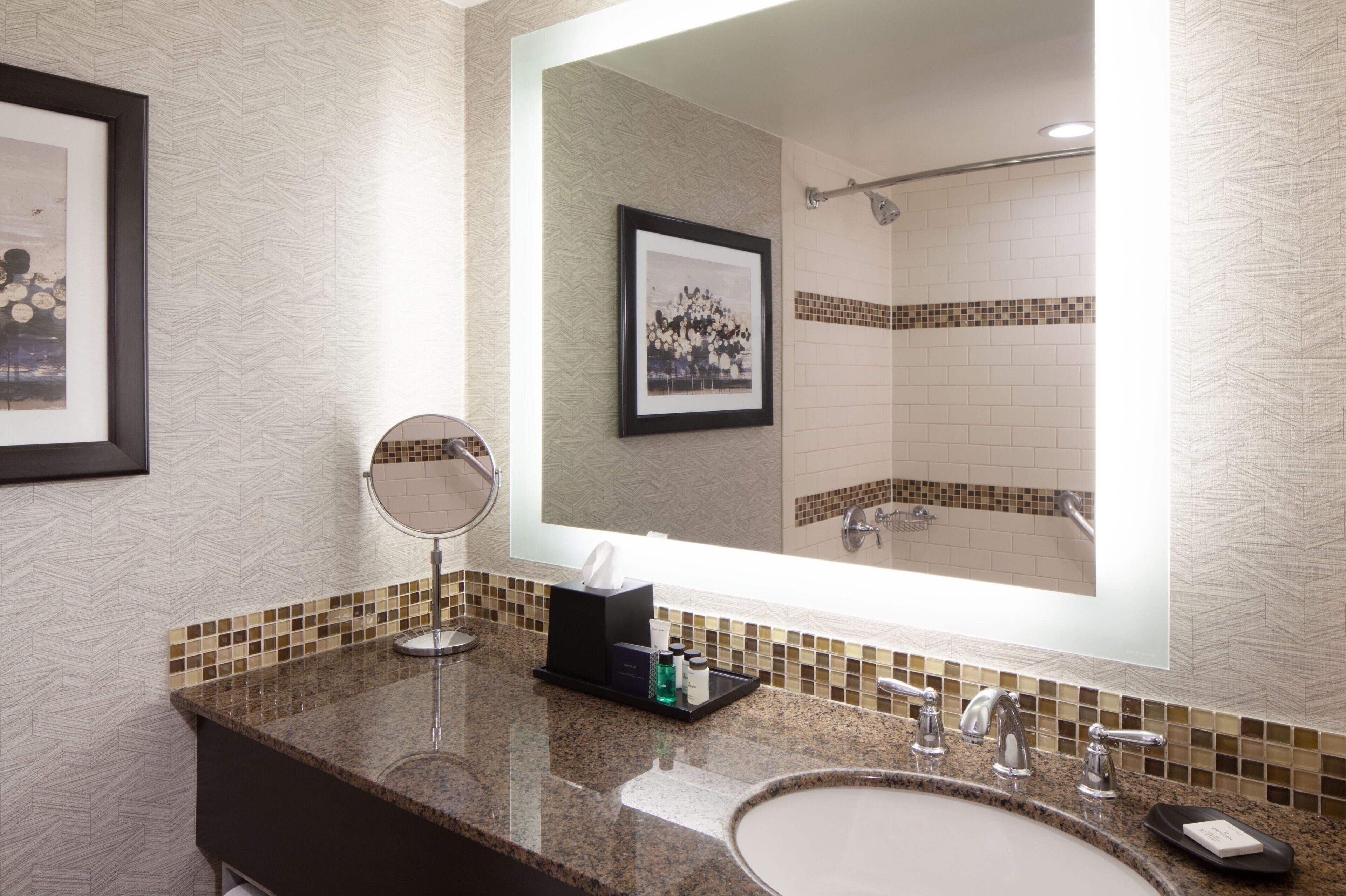 A bathroom with a large mirror, a sink, a framed picture, and a shower area.