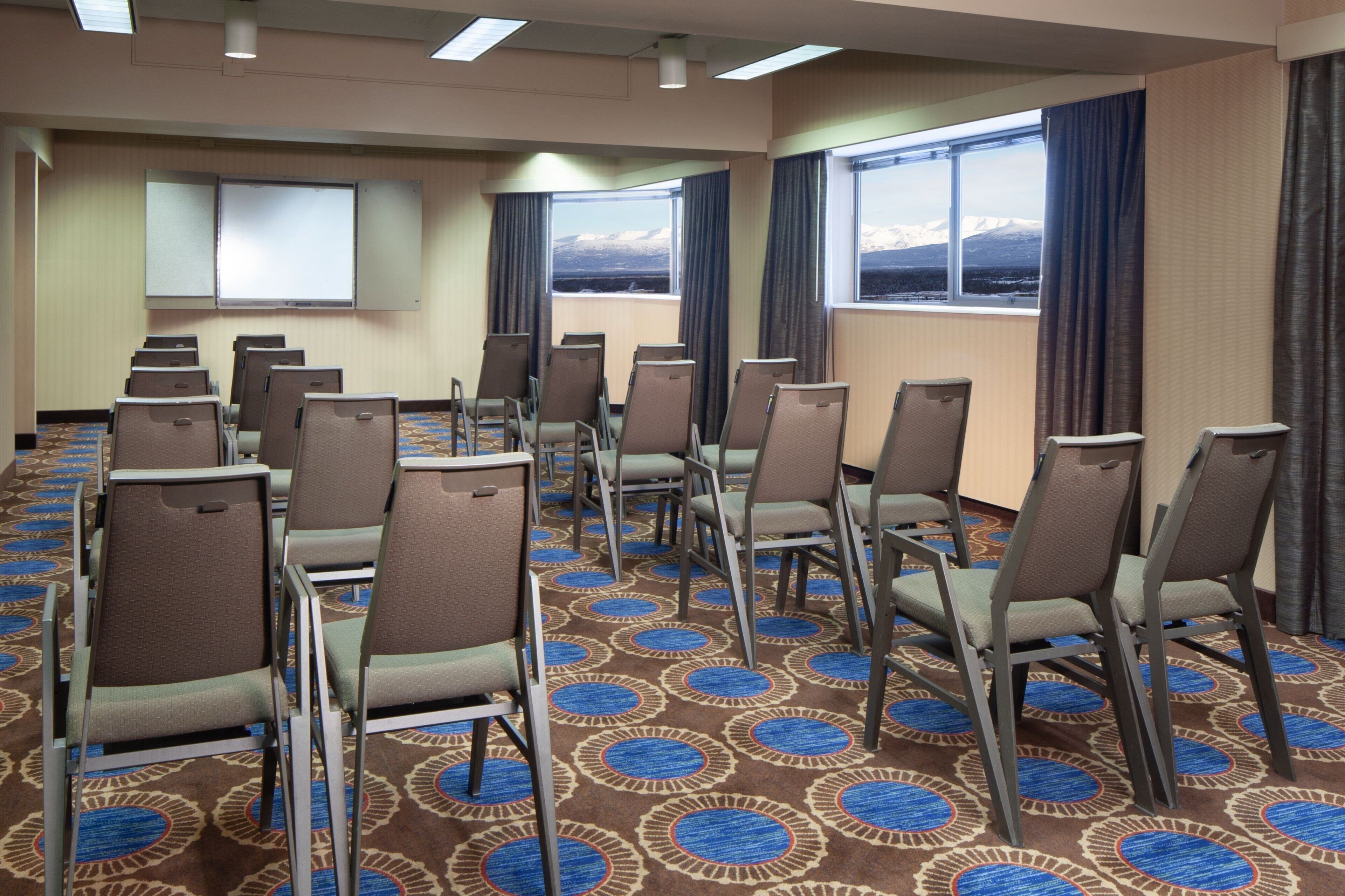 A conference room with rows of chairs, a projector screen, and large windows with a mountain view.