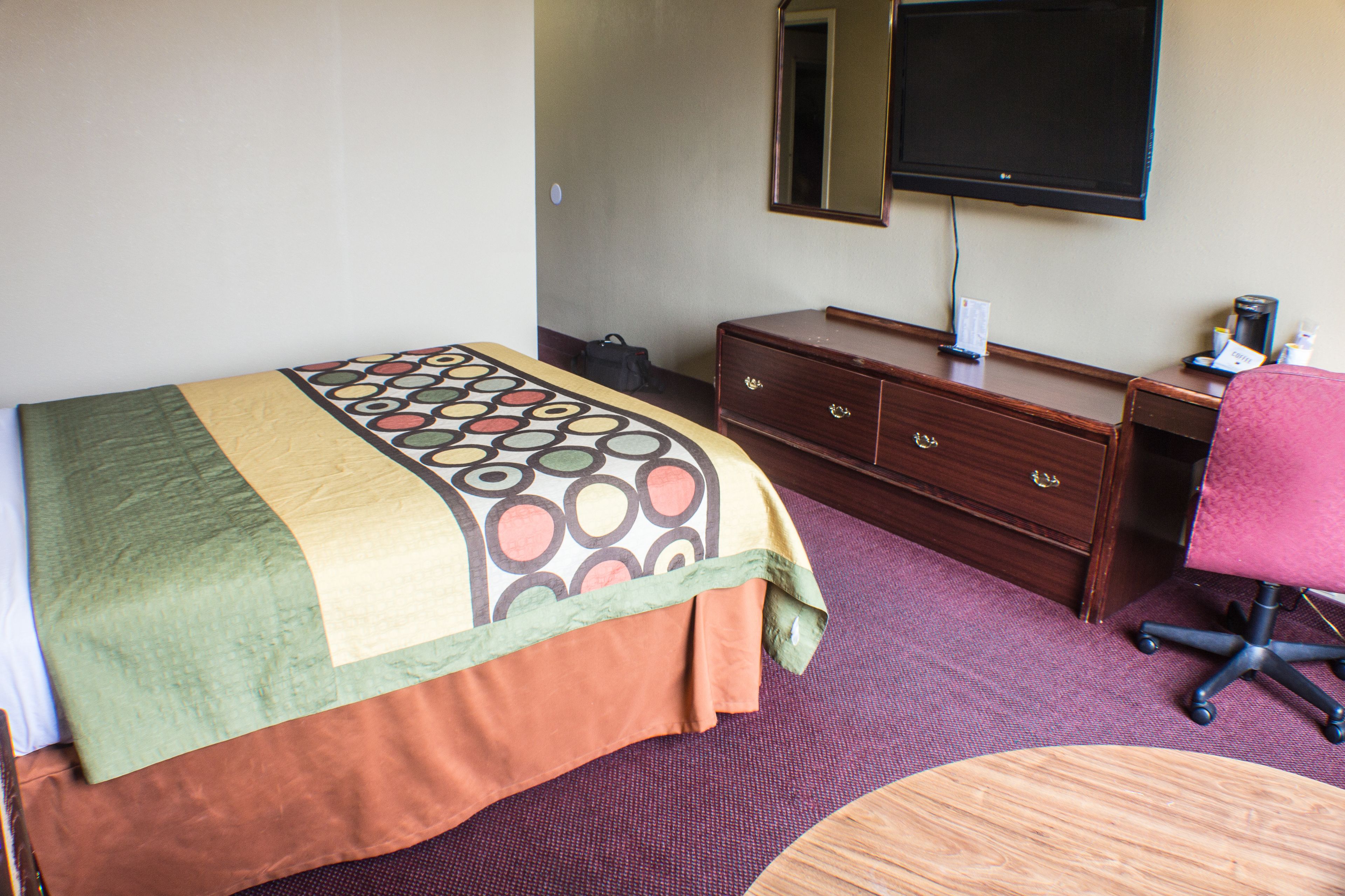A hotel room with a bed, a desk, a chair, a dresser, and a television.