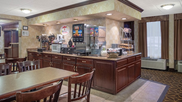 A breakfast bar with a microwave, coffee maker, and a variety of food items. There are wooden chairs and a table with a tiled floor. - Econo Lodge Erie near Casino (Erie)