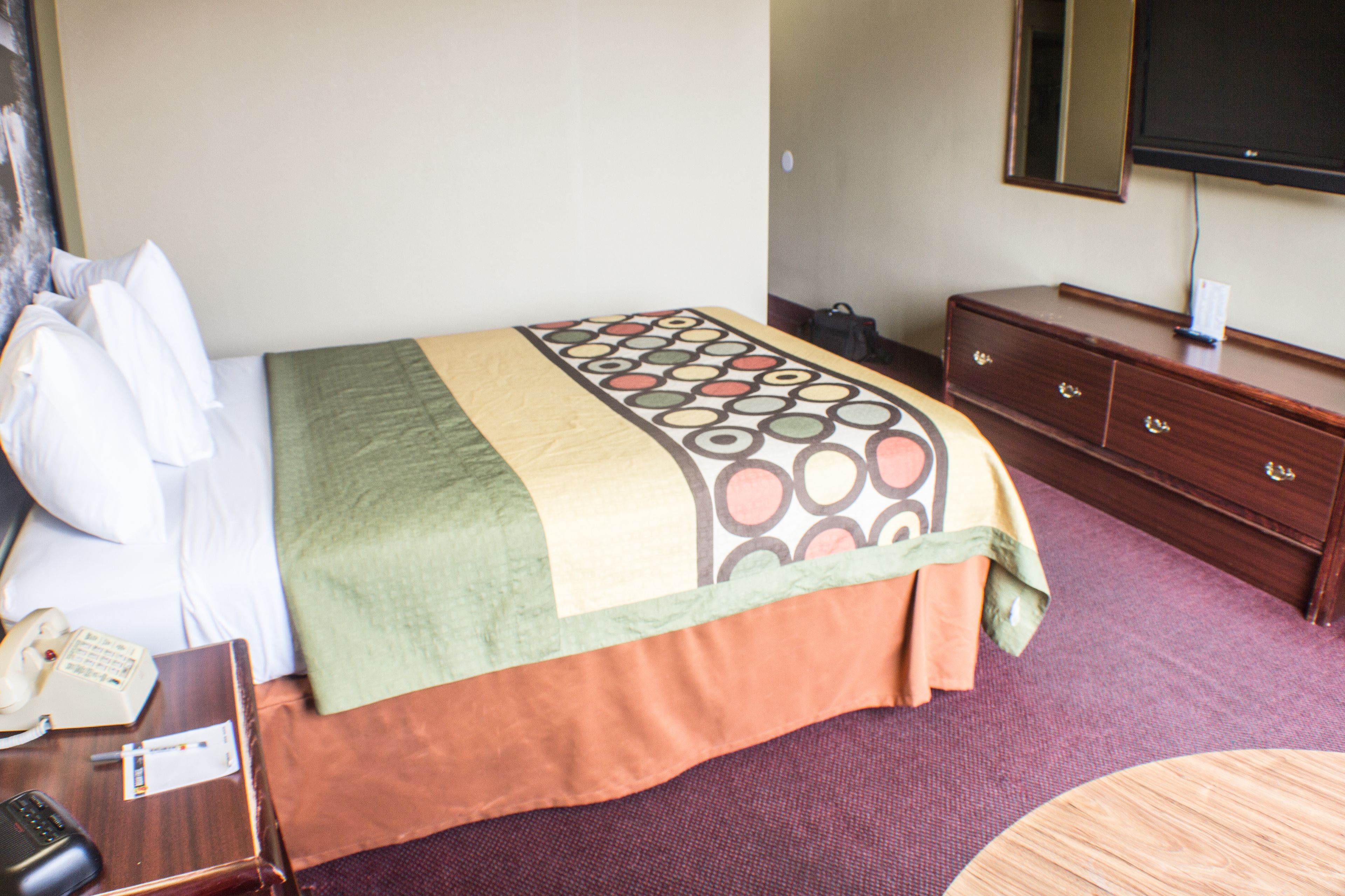 A hotel room with a bed, a wooden dresser, a television, and a telephone on a nightstand.