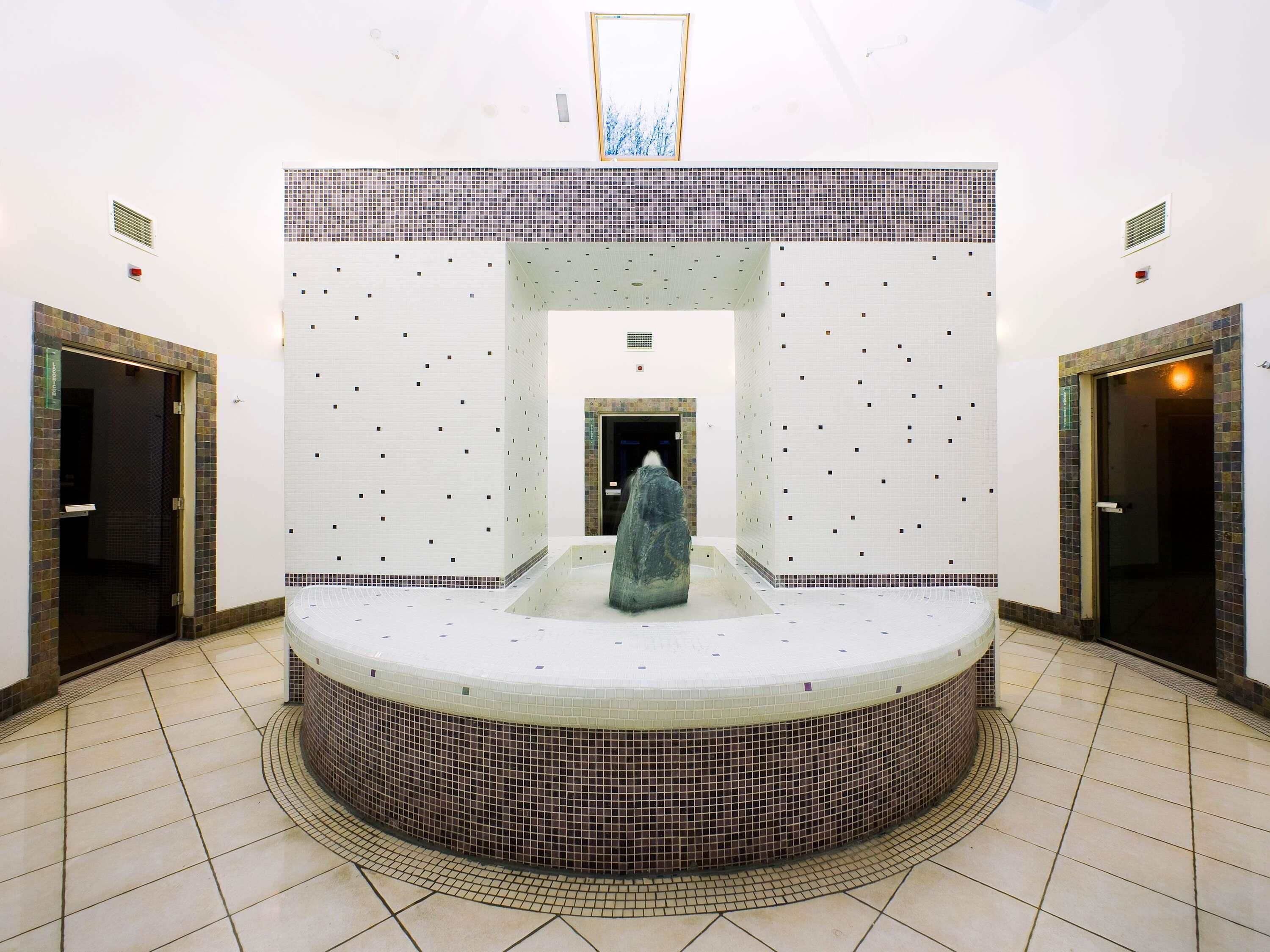 Un área de spa con una bañera de hidromasaje central, paredes y piso azulejados.