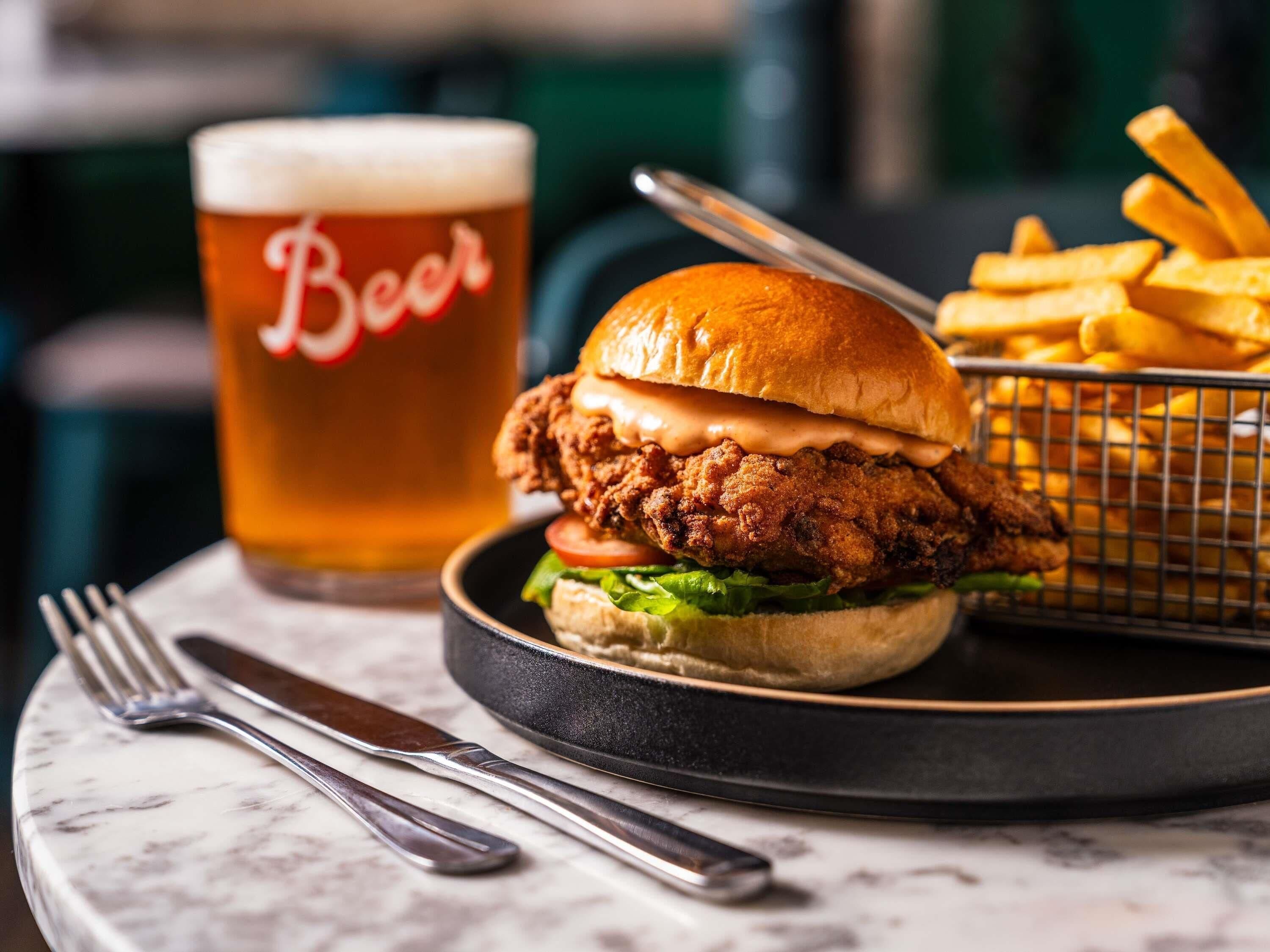 A meal with a fried chicken sandwich, fries, and a beer glass.