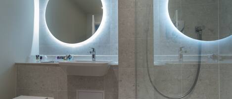 A modern bathroom with a round mirror, a sink, and a shower.
