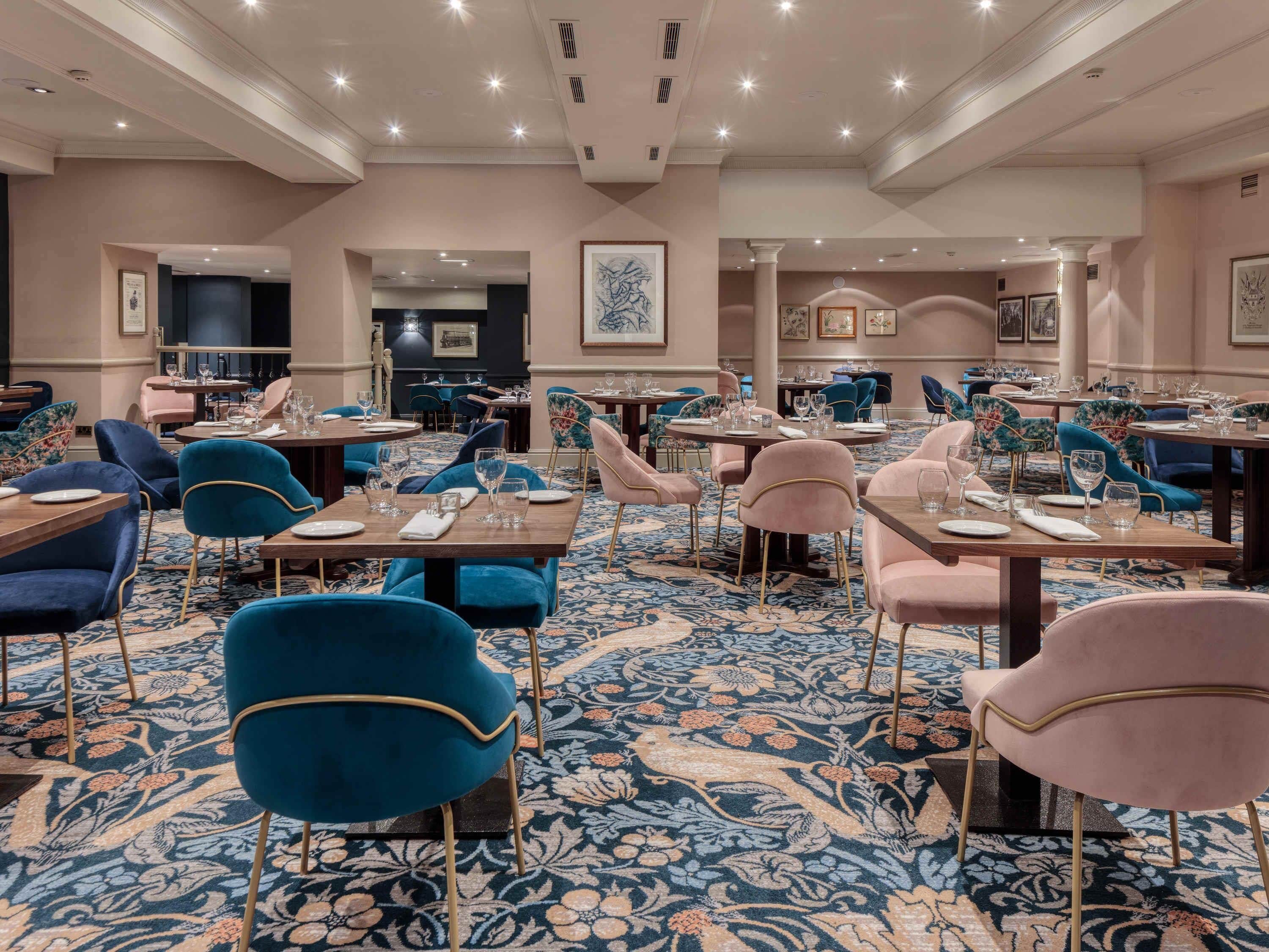 A spacious dining area with round tables and chairs, a patterned carpet, and framed artwork on the walls.