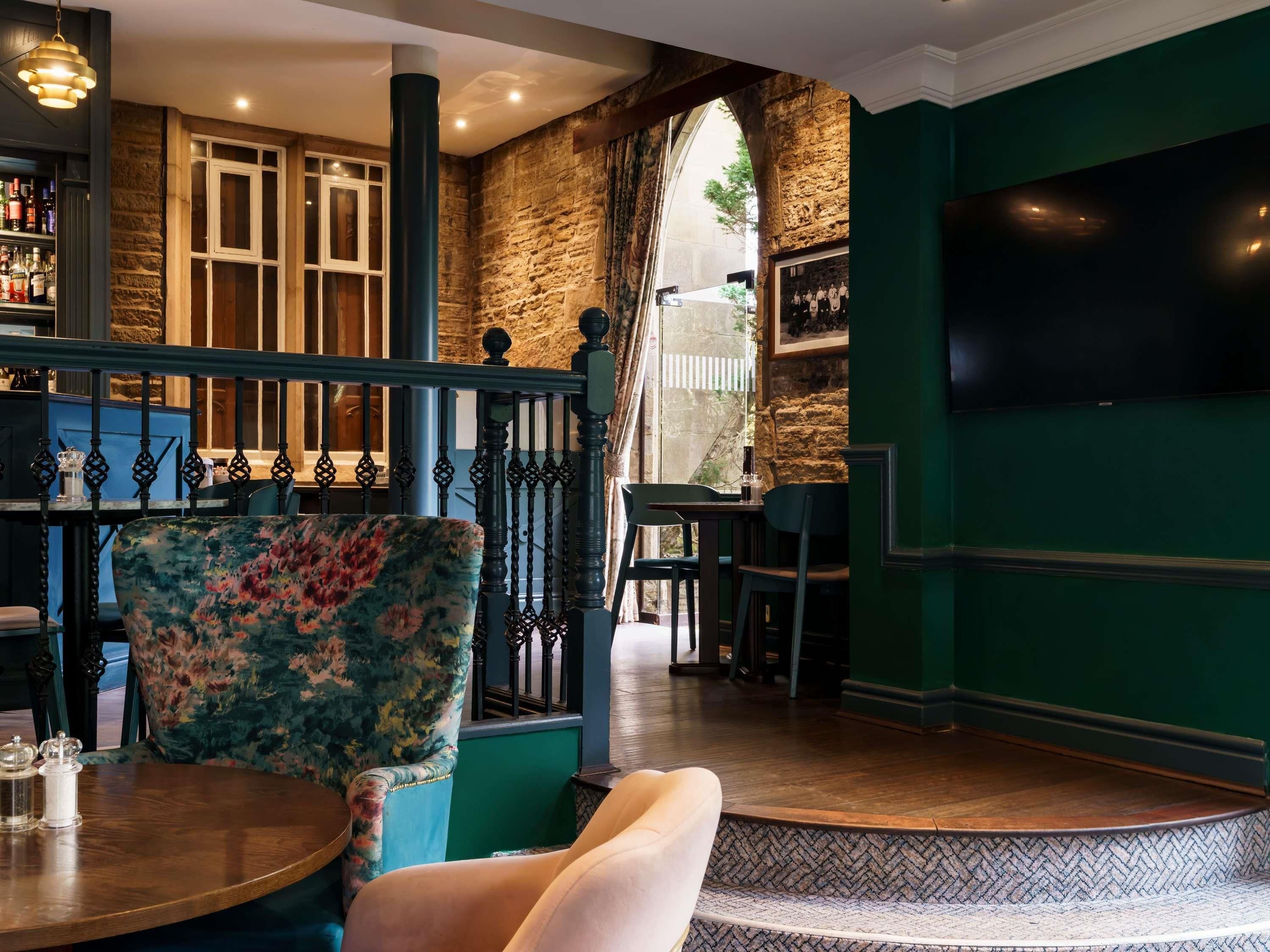 Interior de restaurante con pared de piedra, zona de bar y una disposición de mesas con una mesa redonda y sillas.