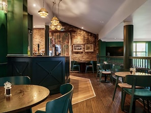 Eine Bar mit Holzboden, grünen Wänden und hängenden Pendelleuchten.