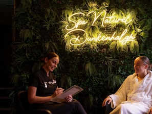 Ein Spa-Ambiente mit einem Neon-Schild mit der Aufschrift 'Spa Naturel Schwankenhalle' und einer Person, die eine Speisekarte hält.