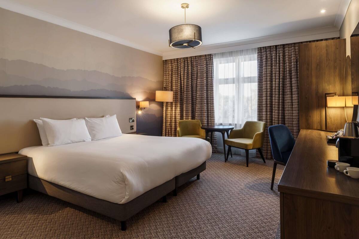 A hotel room with a large bed, two chairs, a desk, and a lamp.