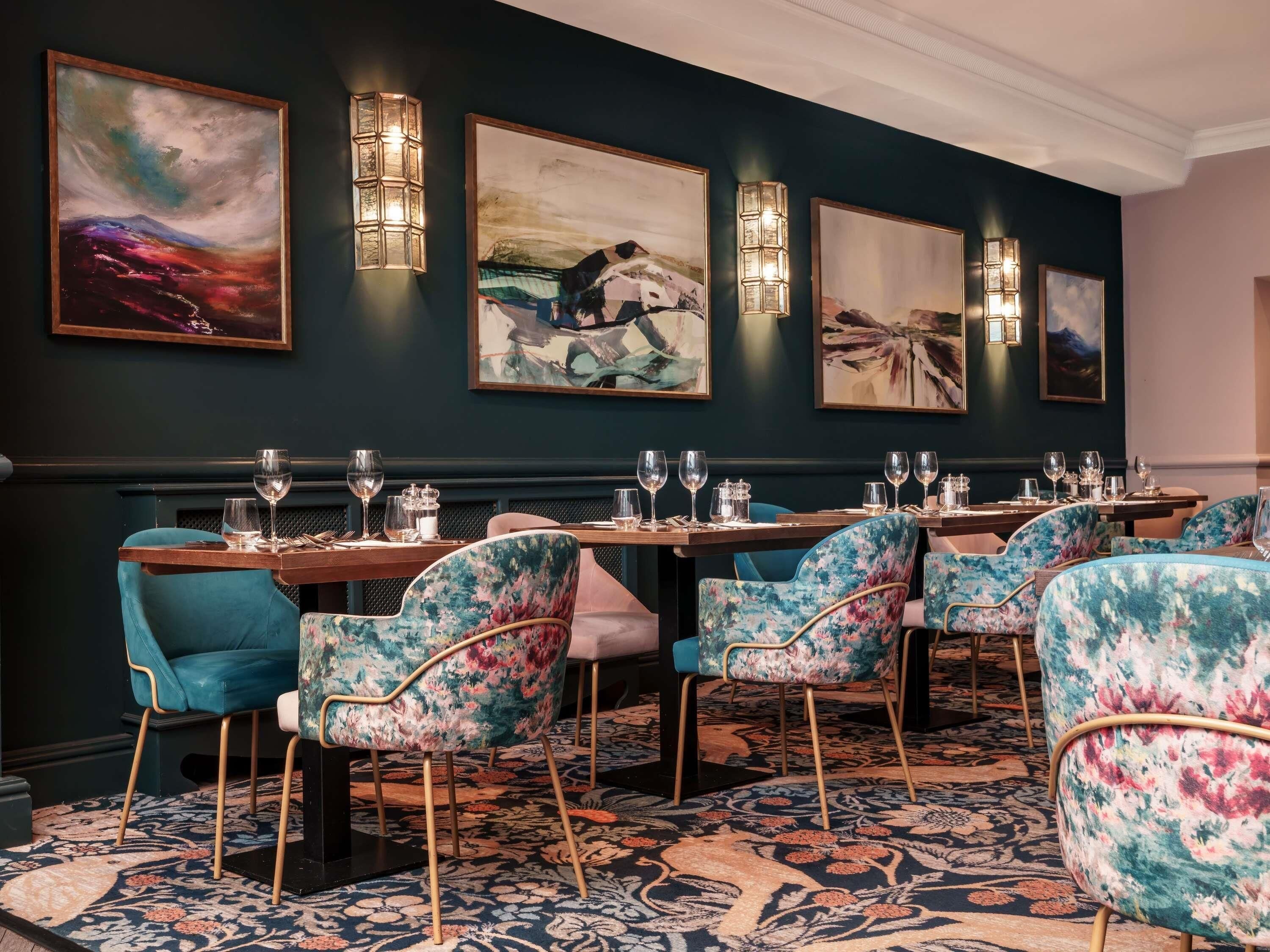 A dining area with tables set for service, chairs upholstered in floral fabric, and artwork on the walls.