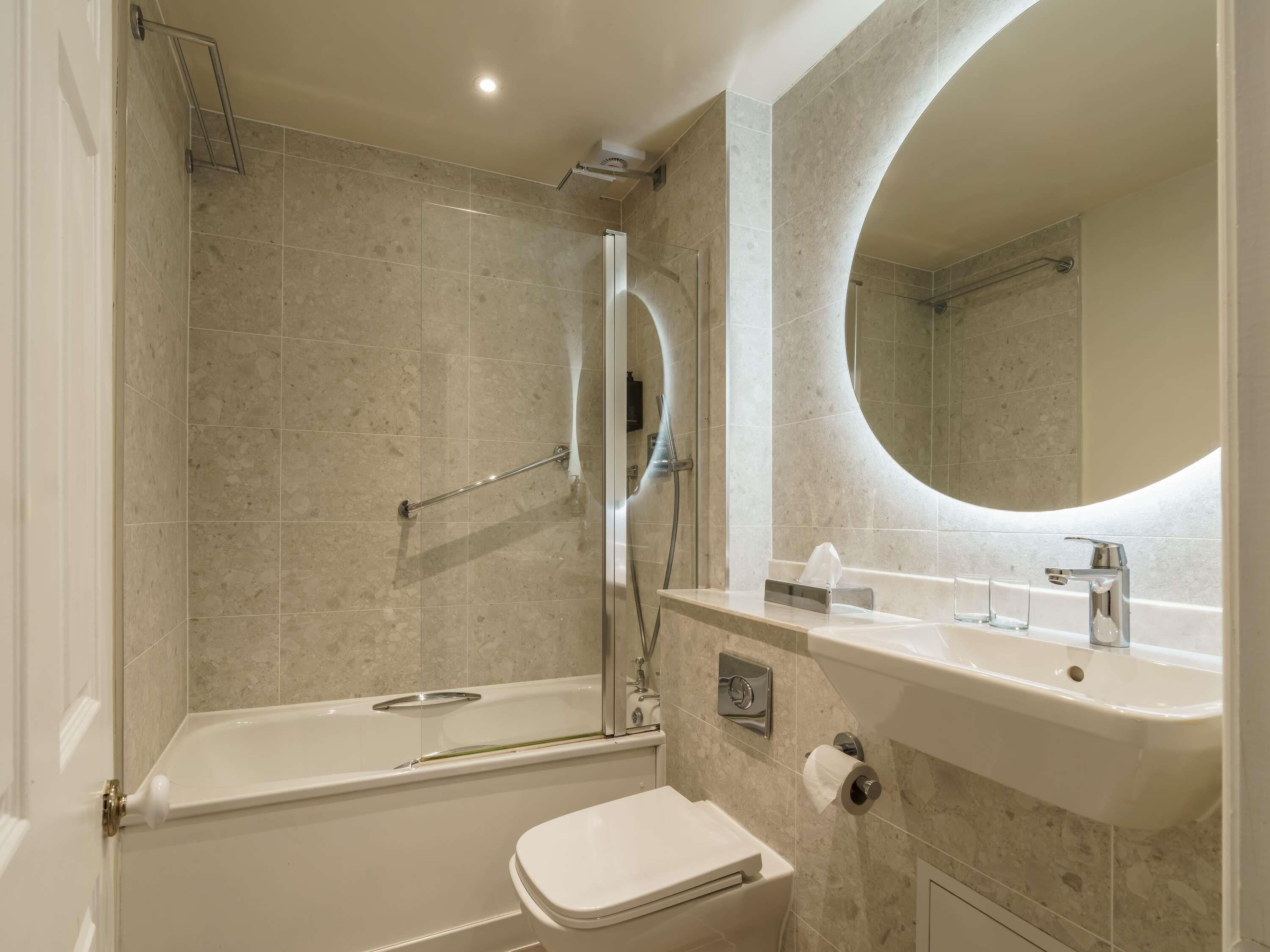 Un baño moderno con bañera, inodoro y un espejo grande.