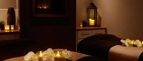 A dimly lit room with two beds, a small table with candles, a mirror, and a decorative vase.