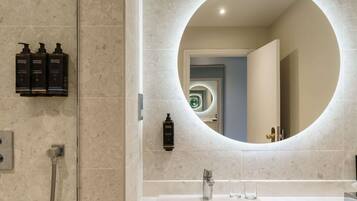 A bathroom with a round mirror, a sink, and three bottles of Elemental Herbology products.