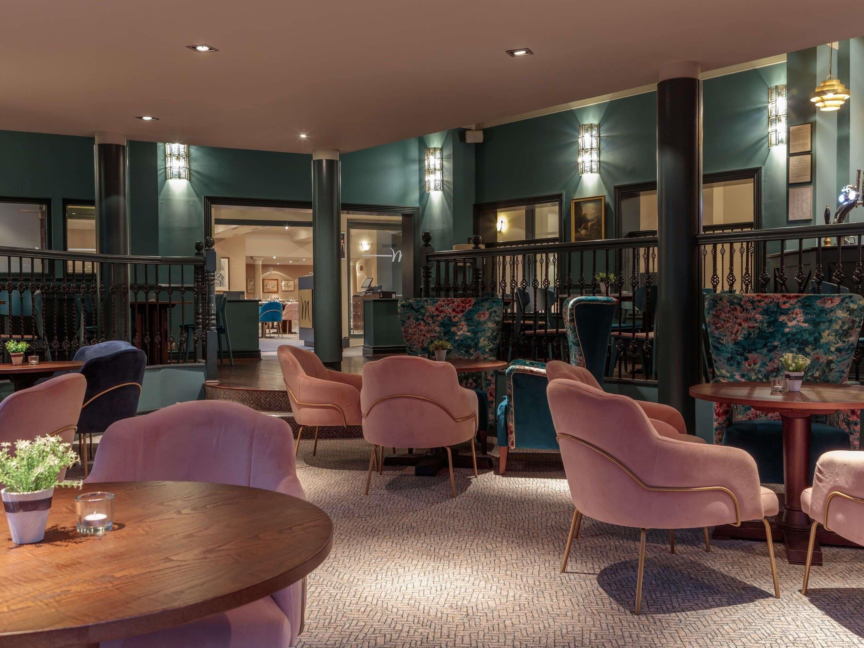 A modern interior with teal walls, wooden flooring, and pink upholstered chairs.